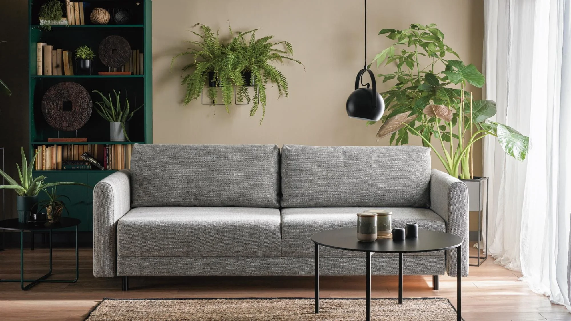 Szara sofa w pokoju z dużą ilością roślin doniczkowych